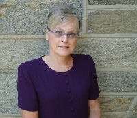 a picture of a woman from head to waist, she is wearing glasses and she has a short hair